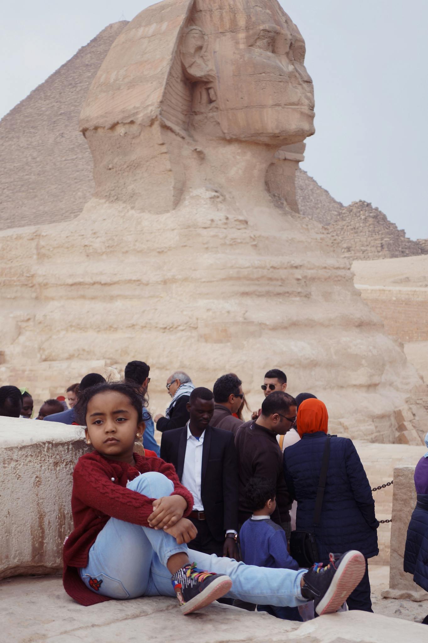 A child poses in front of the Great Sphinx of Giza amid a diverse crowd in Egypt.